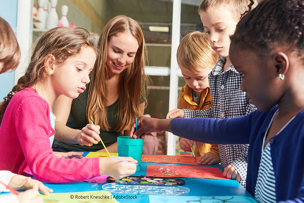 Lehrerin malt mit Schülerinnen und Schülern ein Plakat.
